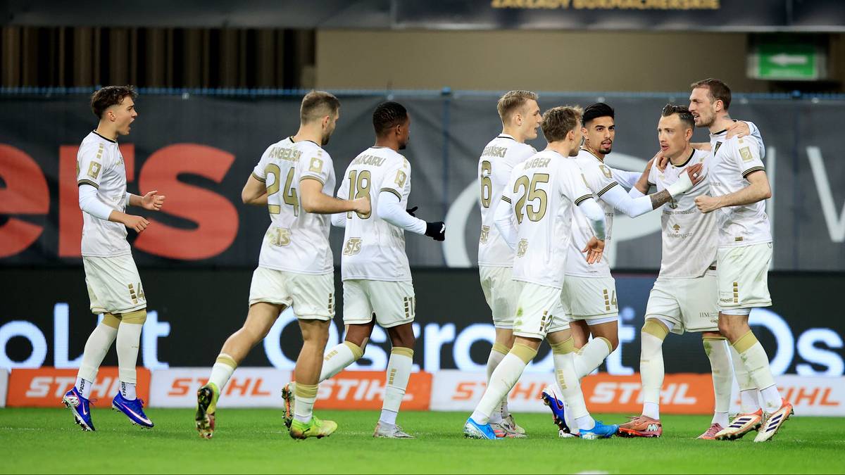 Drużyna piłkarska w białych strojach celebrująca zdobycie punktu na boisku.