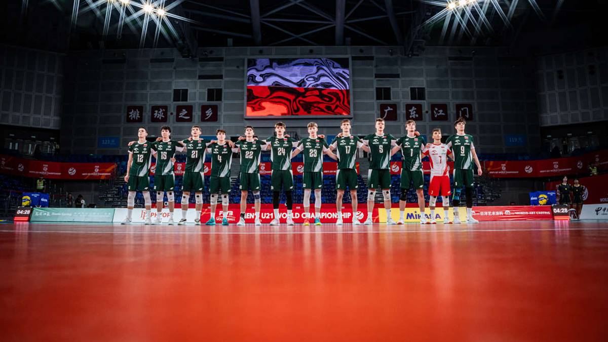 Drużyna siatkarzy w zielonych strojach pozuje do zdjęcia na tle trybun hali sportowej.