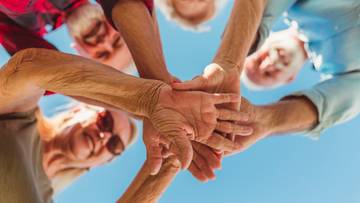 Grupa starszych os&oacute;b łącząca ręce w geście jedności.
