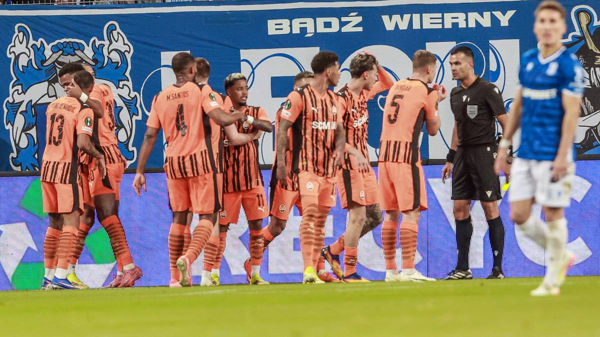 Piłkarze Szachtara Donieck w pomarańczowych strojach świętują na boisku, w tle kibice na trybunach.