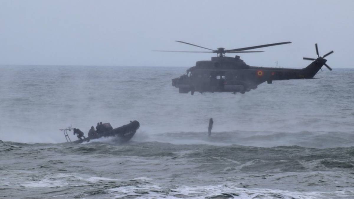 Wojskowy śmigłowiec i łódź na wzburzonym morzu.