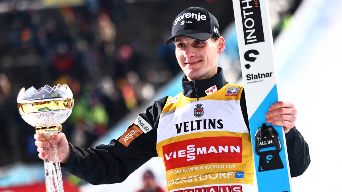 Skoczek narciarski prezentuje trofeum i nartę.