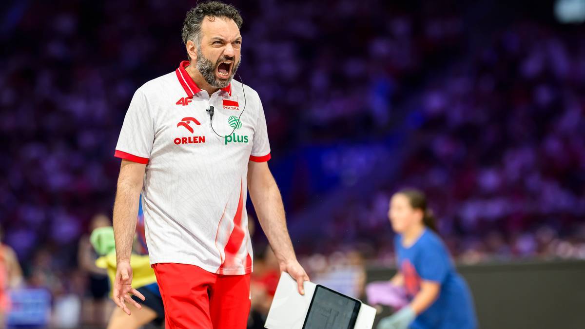 Trener siatk&oacute;wki w białej koszulce z czerwonymi pasami i czerwonych spodenkach, krzyczący i trzymający tablet.