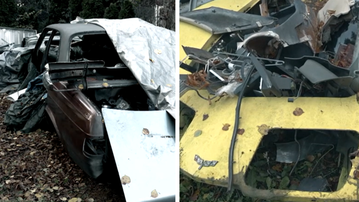 Zniszczone karoserie i części samochodowe leżące na ziemi, przykryte plandeką lub rozrzucone w nieładzie.