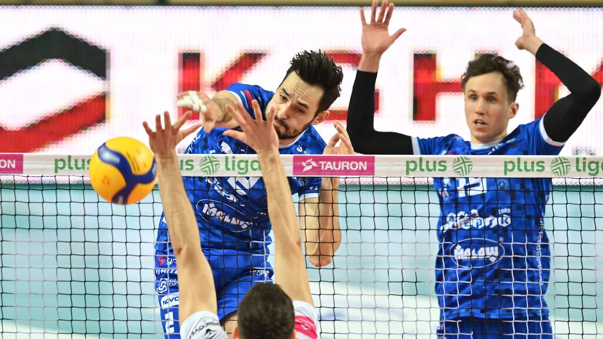 Siatkarz w niebieskiej koszulce wykonuje blok, próbując zatrzymać piłkę podczas meczu Plus Ligi.