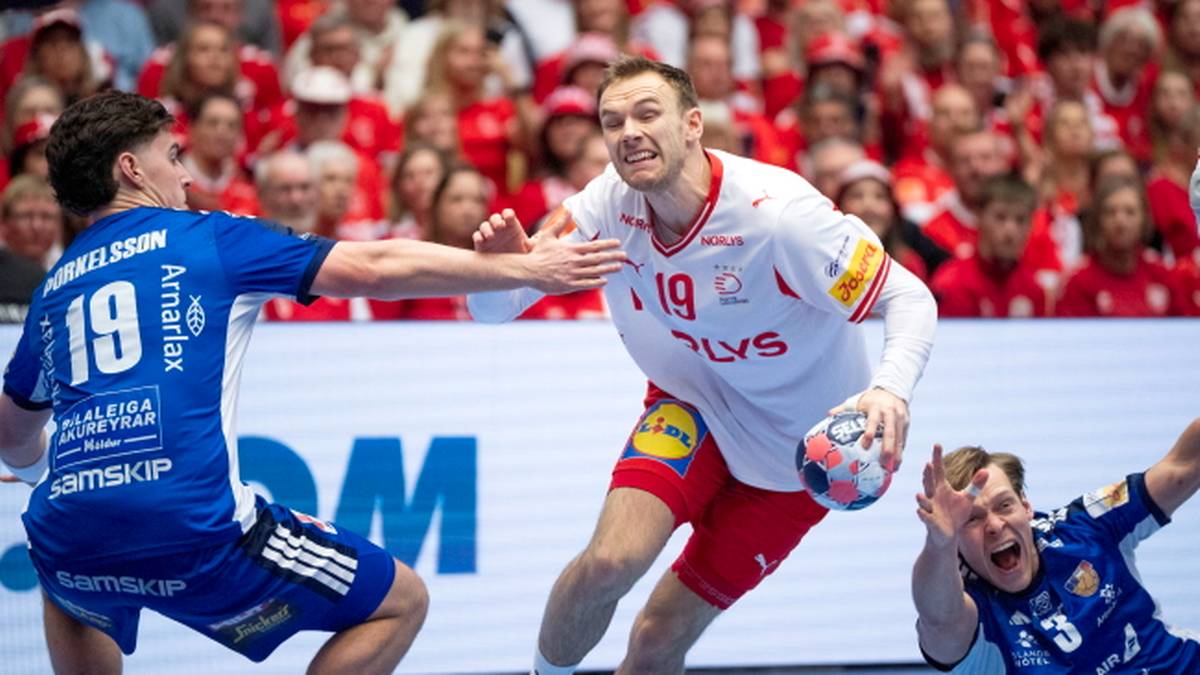 Piłkarz ręczny w białej koszulce z numerem 19 pr&oacute;buje rzucić piłkę, broni go zawodnik w niebieskiej koszulce.