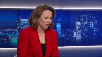 Kobieta w czerwonej marynarce z kr&oacute;tkimi, brązowymi włosami, m&oacute;wiąca do mikrofonu, na tle ekranu z nocnym widokiem miasta.