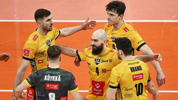 Siatkarze w żółtych strojach celebrują zdobyty punkt, jeden z nich jest w szarym stroju.