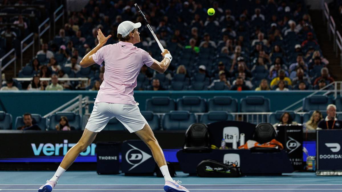 Tenisista wykonuje uderzenie podczas meczu, widownia na trybunach w tle.