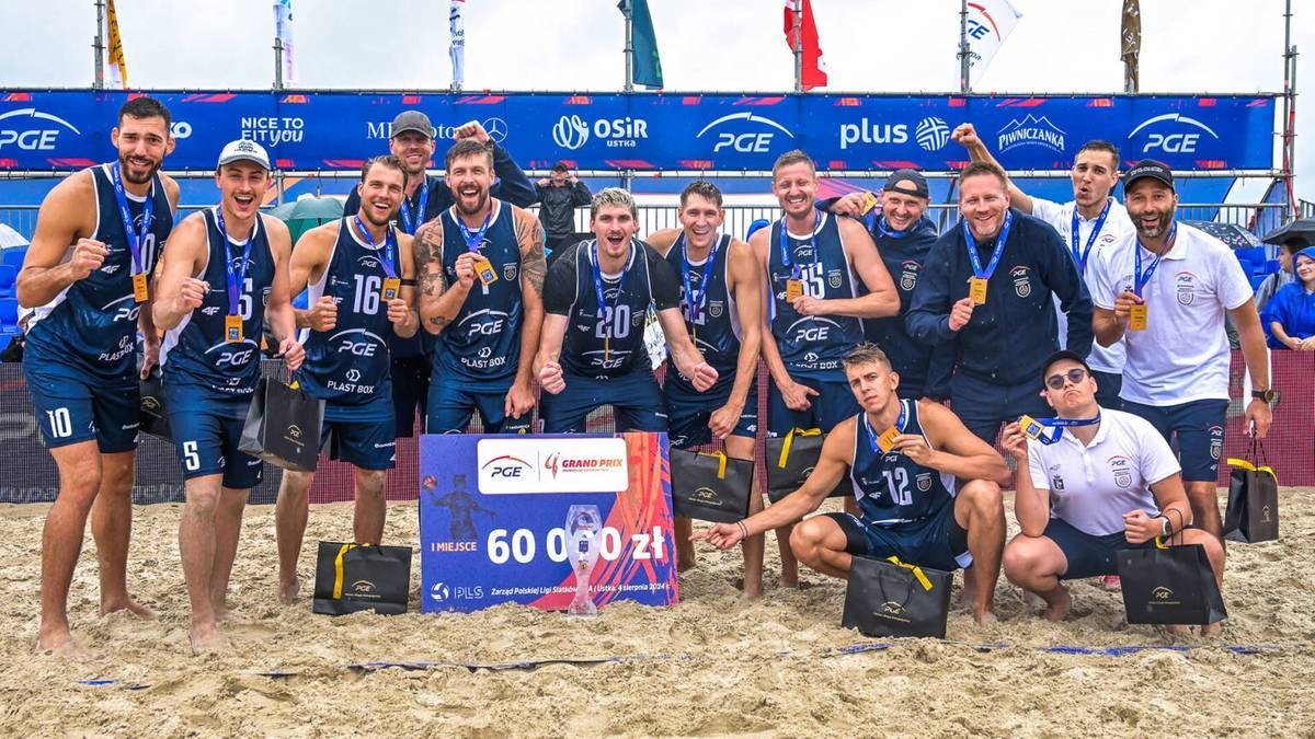 Drużyna siatkarzy w strojach sportowych pozuje do zdjęcia z medalem na szyi i pucharem w rękach, stojąc na plaży przed tablicą z napisem "60 000 zł".