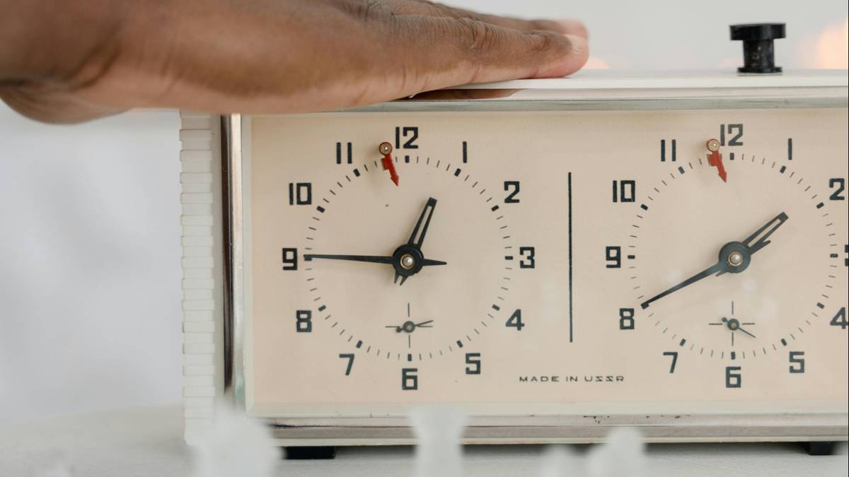 Dłoń spoczywa na klasycznym zegarze szachowym z dwiema tarczami wskazującymi różne godziny.
