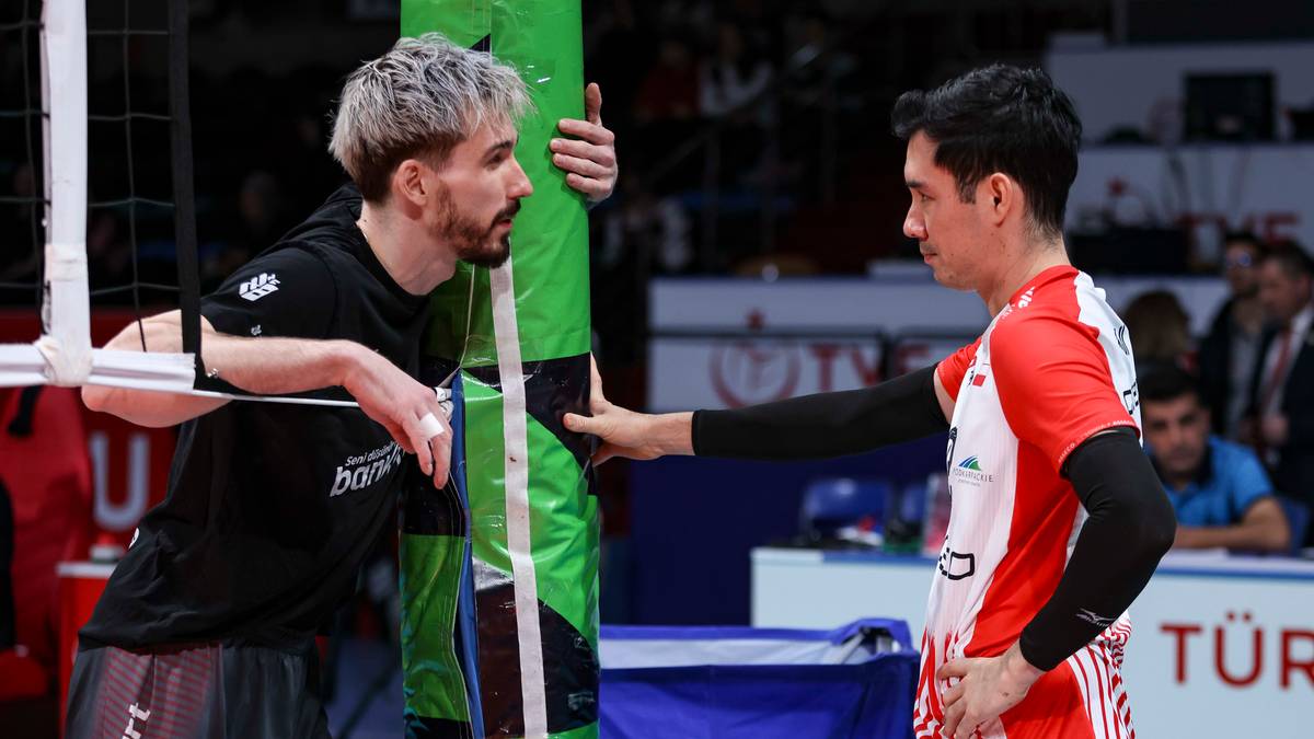 Dw&oacute;ch siatkarzy w sportowych strojach rozmawia przy siatce podczas meczu siatk&oacute;wki.