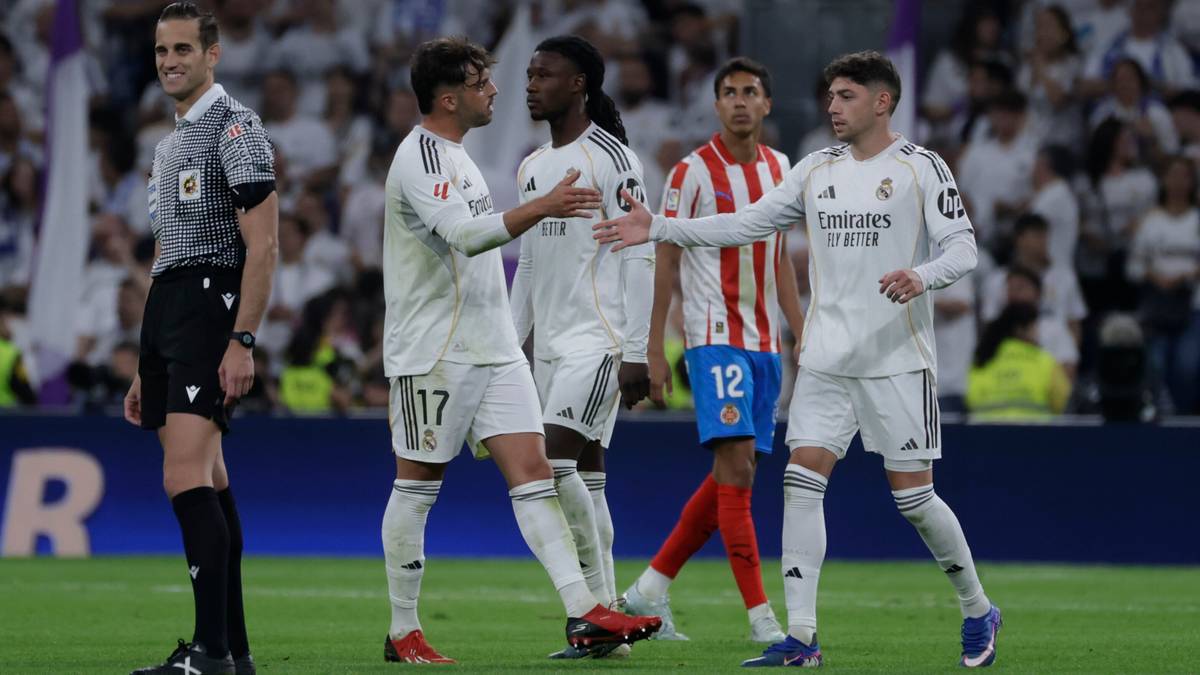 Piłkarze Realu Madryt rozmawiający na boisku podczas meczu, z kibicami na trybunach w tle.