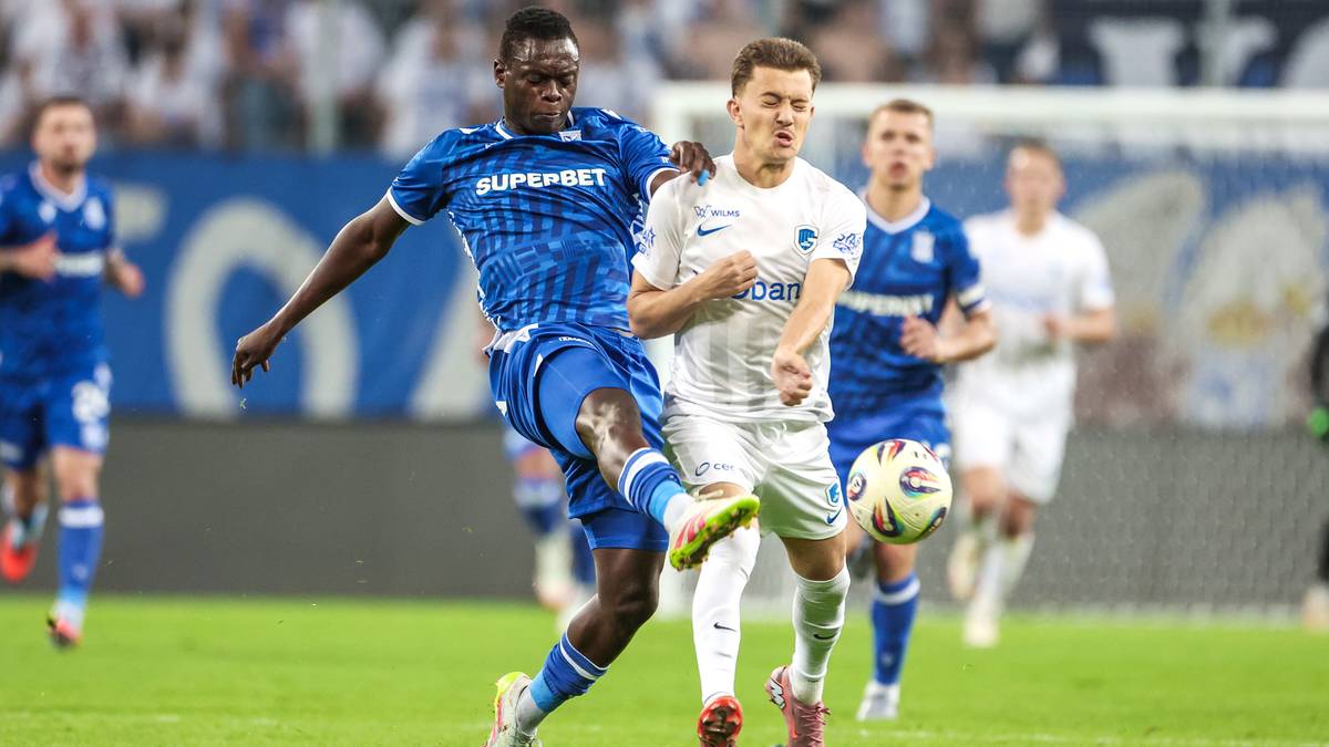 Dwóch piłkarzy walczących o piłkę na boisku, jeden w niebieskim stroju, drugi w białym.