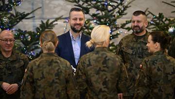 Szef MON wraz z żołnierzami w świątecznej atmosferze, z choinkami w tle.
