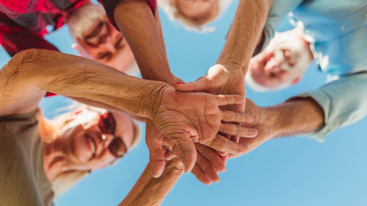 Grupa starszych os&oacute;b łącząca ręce w geście jedności.