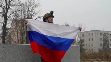 Żołnierz w hełmie i mundurze trzyma rozłożoną flagę Rosji.