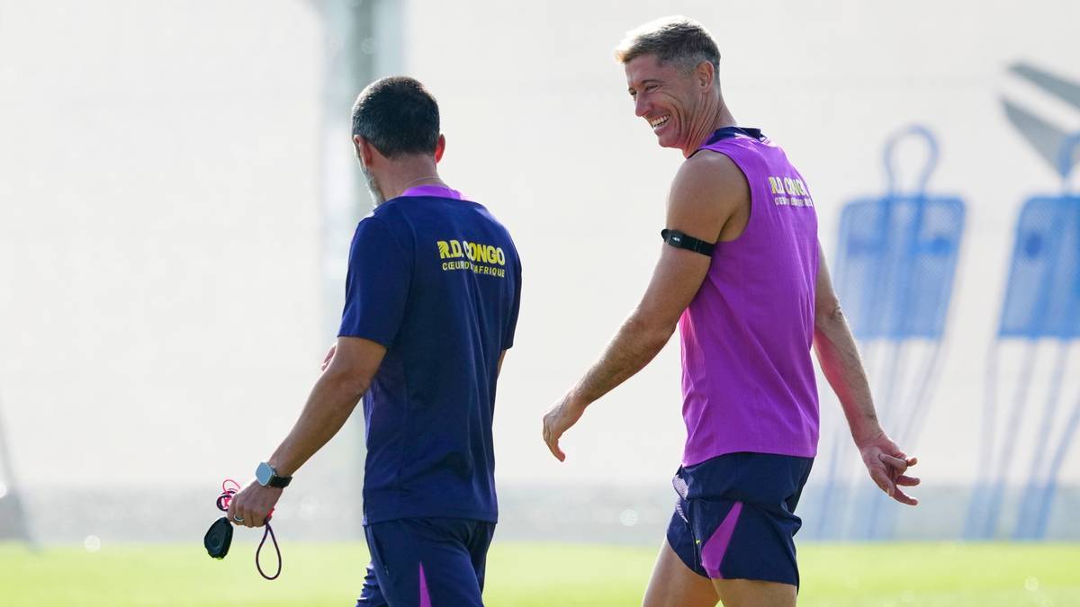 Robert Lewandowski idzie po boisku treningowym obok członka sztabu, obaj ubrani w stroje sportowe.