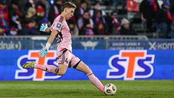 Piłkarz Rakowa Częstochowa w r&oacute;żowej koszulce i spodenkach, w ż&oacute;łtych rękawicach bramkarskich, wykonuje zagranie nogą do piłki.