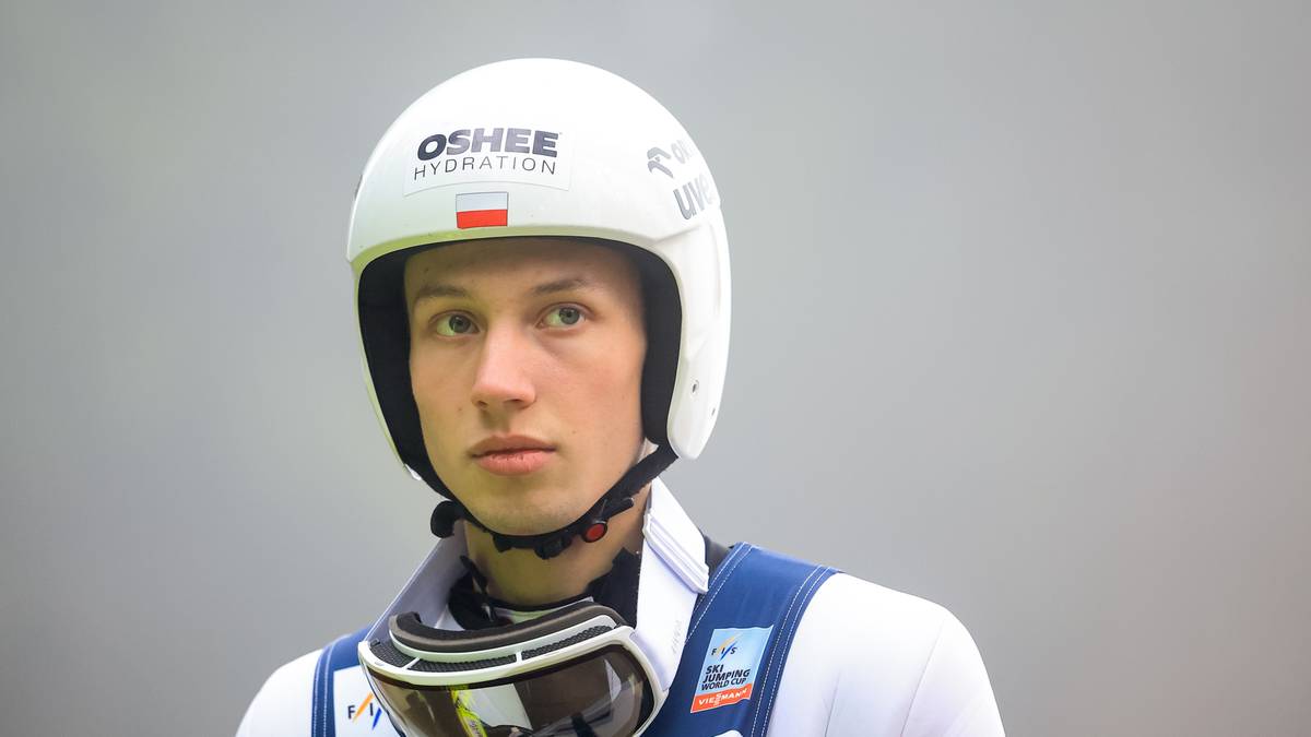 Portret skoczka narciarskiego w białym kasku i goglach narciarskich.