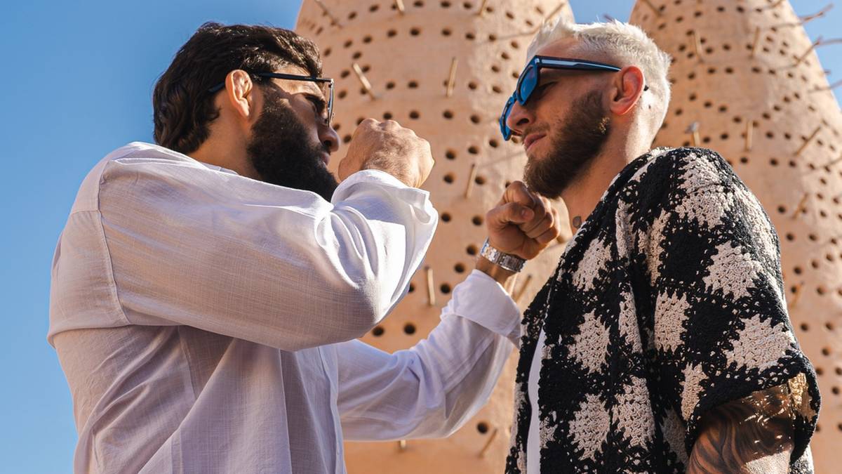 Dwóch mężczyzn, potencjalnie zawodnicy MMA, w okularach przeciwsłonecznych i z zarostem, stoją naprzeciwko siebie i dotykają się splecionymi dłońmi.