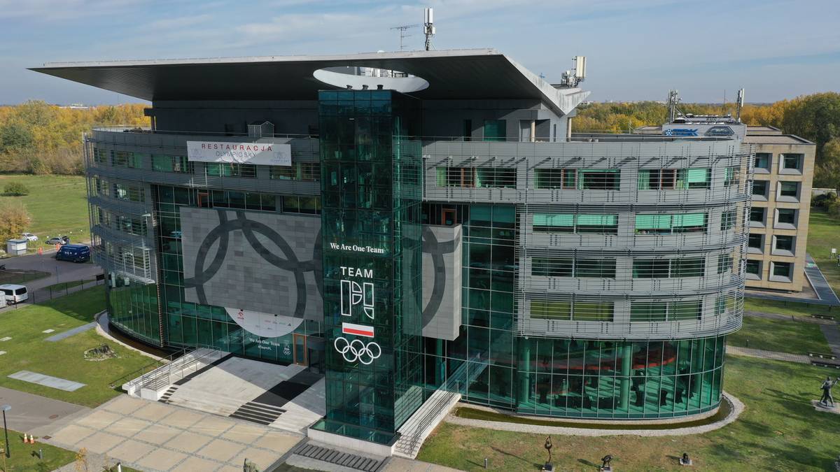 Nowoczesny budynek Polskiego Komitetu Olimpijskiego z dużymi, szklanymi elementami i logo olimpijskim.
