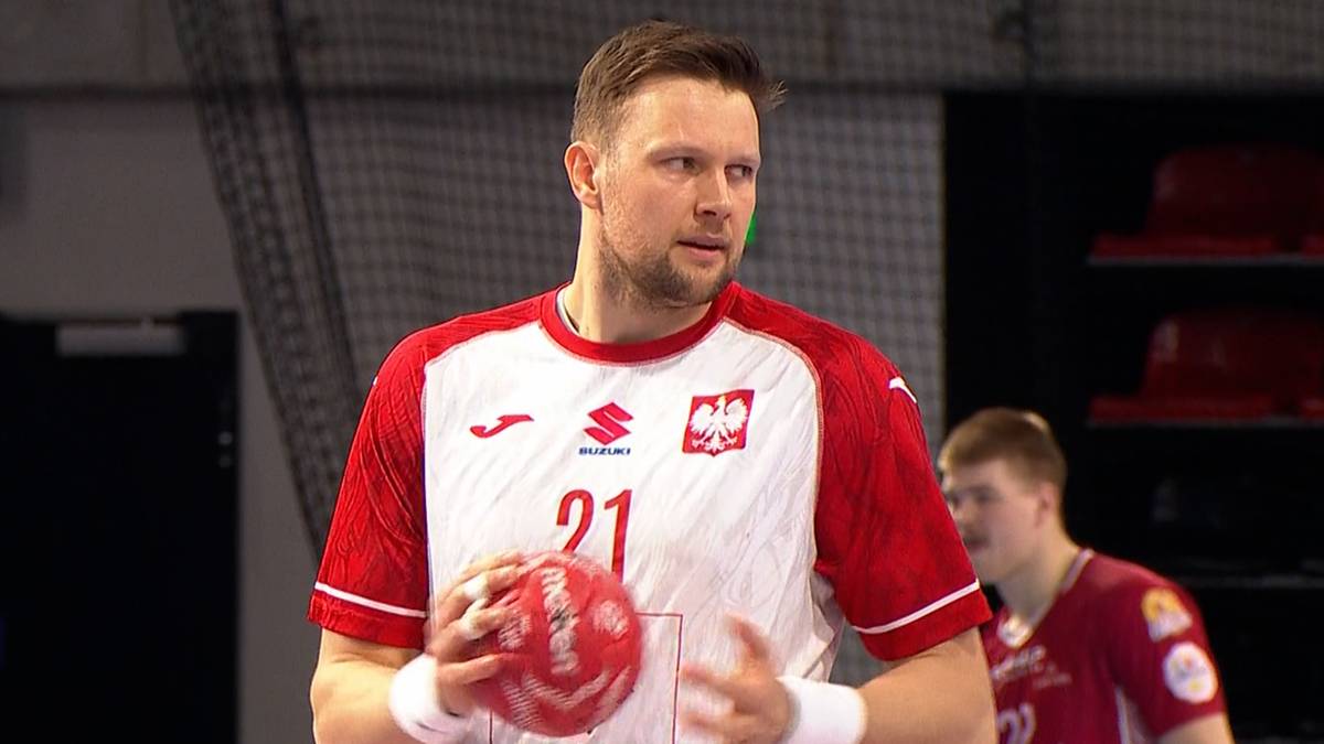 Polski zawodnik w czerwono-białej koszulce z numerem 21 i godłem Polski, trzymający czerwoną piłkę do piłki ręcznej.