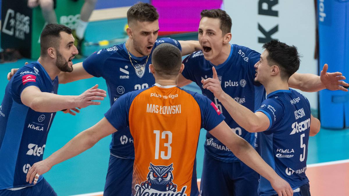 Pięciu siatkarzy w niebieskich strojach wpatruje się w jednego zawodnika w pomarańczowym stroju z numerem 13 na plecach, gestykulując i okazując emocje.