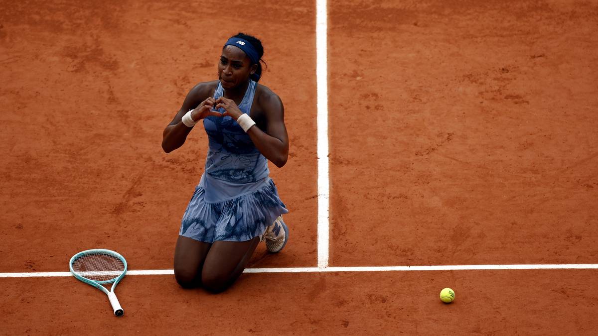 Tenisistka w niebieskiej sukience na kolanach na kortach Rolanda Garrosa, celebrująca zwycięstwo. Obok niej leży rakieta, a w oddali widać piłkę.