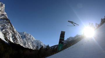Skoczek narciarski w locie nad ośnieżoną g&oacute;rą.