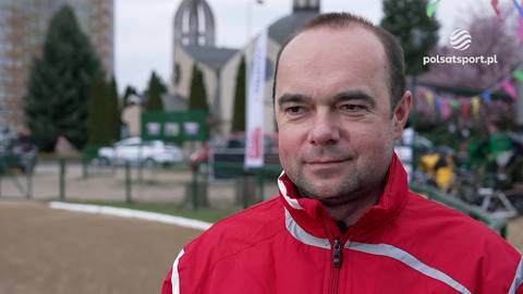 Tomasz Pokorski w czerwonej kurtce sportowej, patrzący przed siebie.