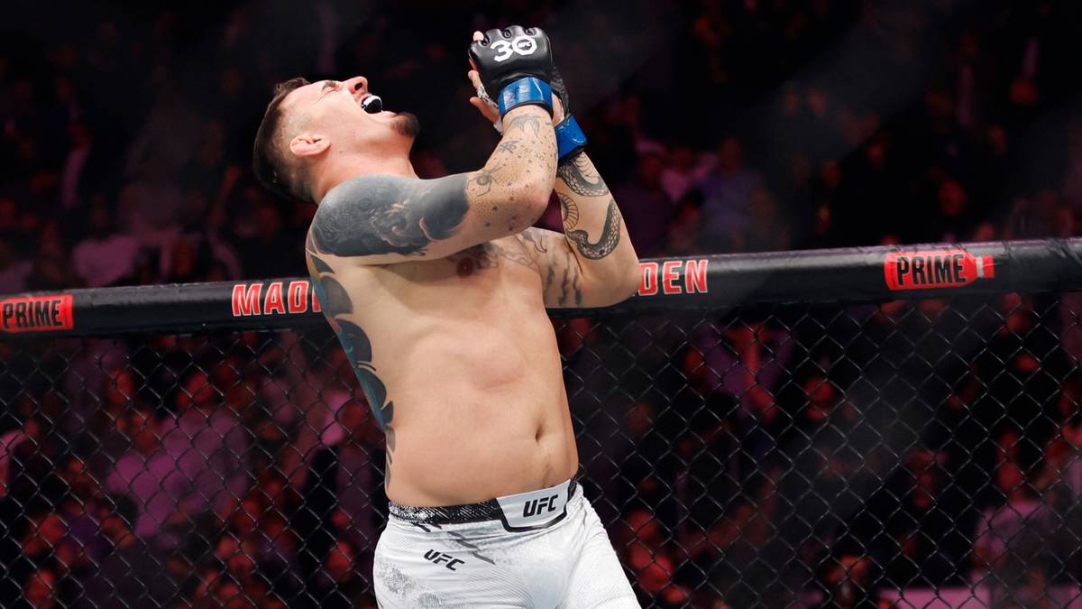 Zawodnik MMA w rękawicach i spodenkach UFC unosi ręce w geście triumfu, krzycząc z radości na tle publiczności i ringu.