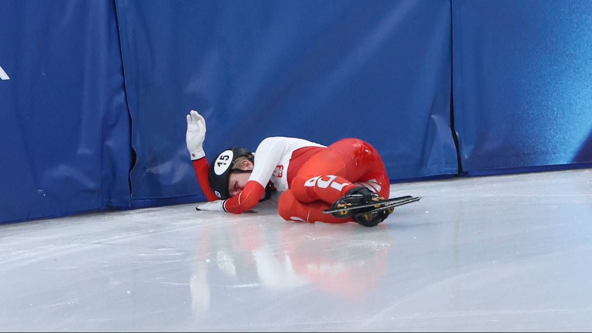 Zawodniczka short tracku w czerwonym stroju leży na lodzie po upadku.