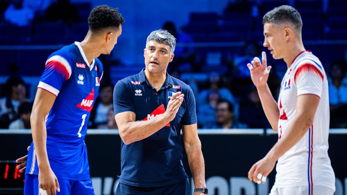 Siatkarz w niebieskim stroju rozmawia z trenerem, obok stoi siatkarz w białym stroju.