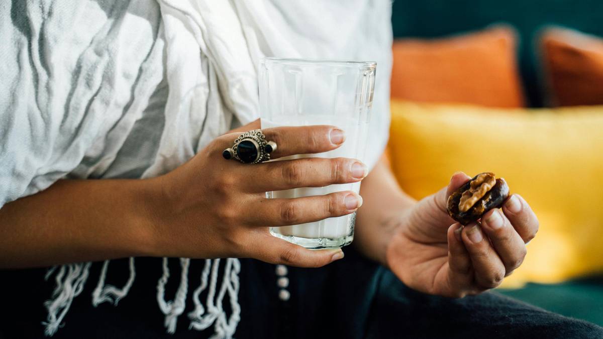 Dłoń trzymająca szklankę z białym płynem i daktyla nadziewanego orzechami.