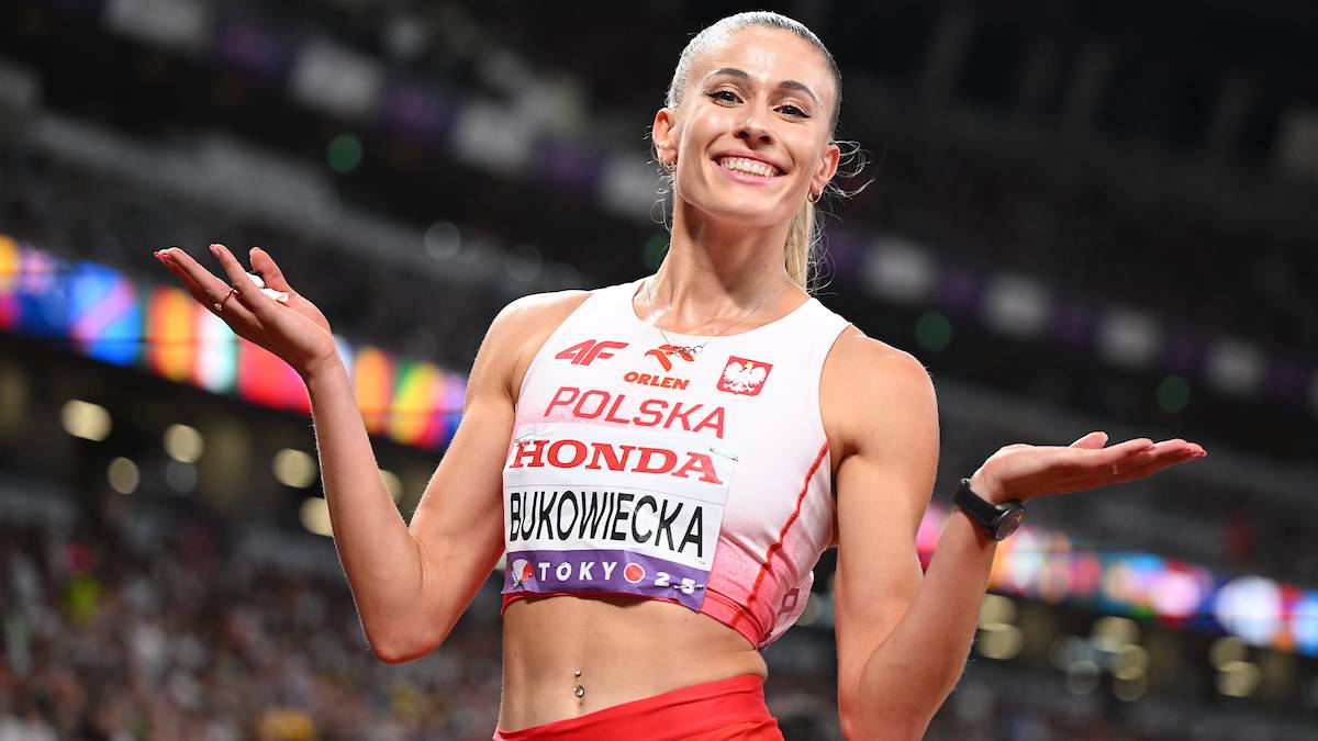 Uśmiechnięta lekkoatletka w stroju sportowym z napisem Polska, pokazuje ręce na boki.