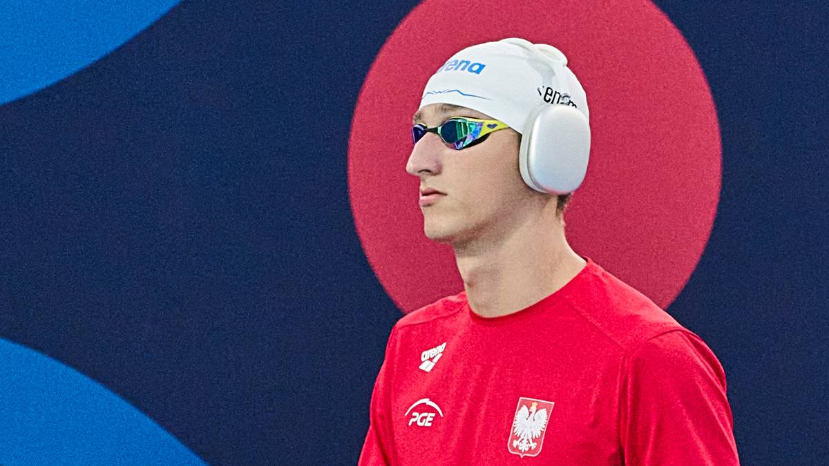 Młody mężczyzna w czepku pływackim, goglach i słuchawkach pływackich, ubrany w czerwoną koszulkę sportową z polskim godłem.