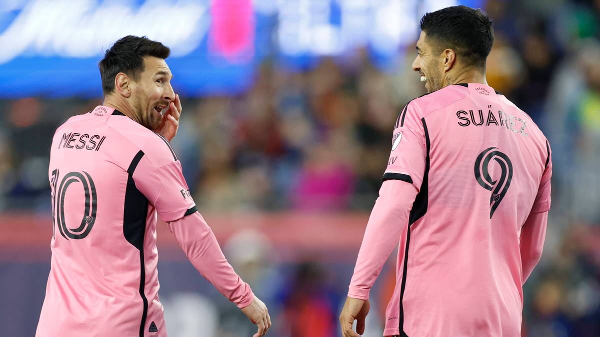 Dwóch piłkarzy w różowych koszulkach: Messi (z numerem 10) i Suarez (z numerem 9). Obaj patrzą na siebie i rozmawiają, na boisku piłkarskim.