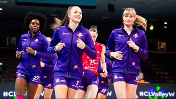 Trzy siatkarki w fioletowych strojach sportowych biegną po boisku.