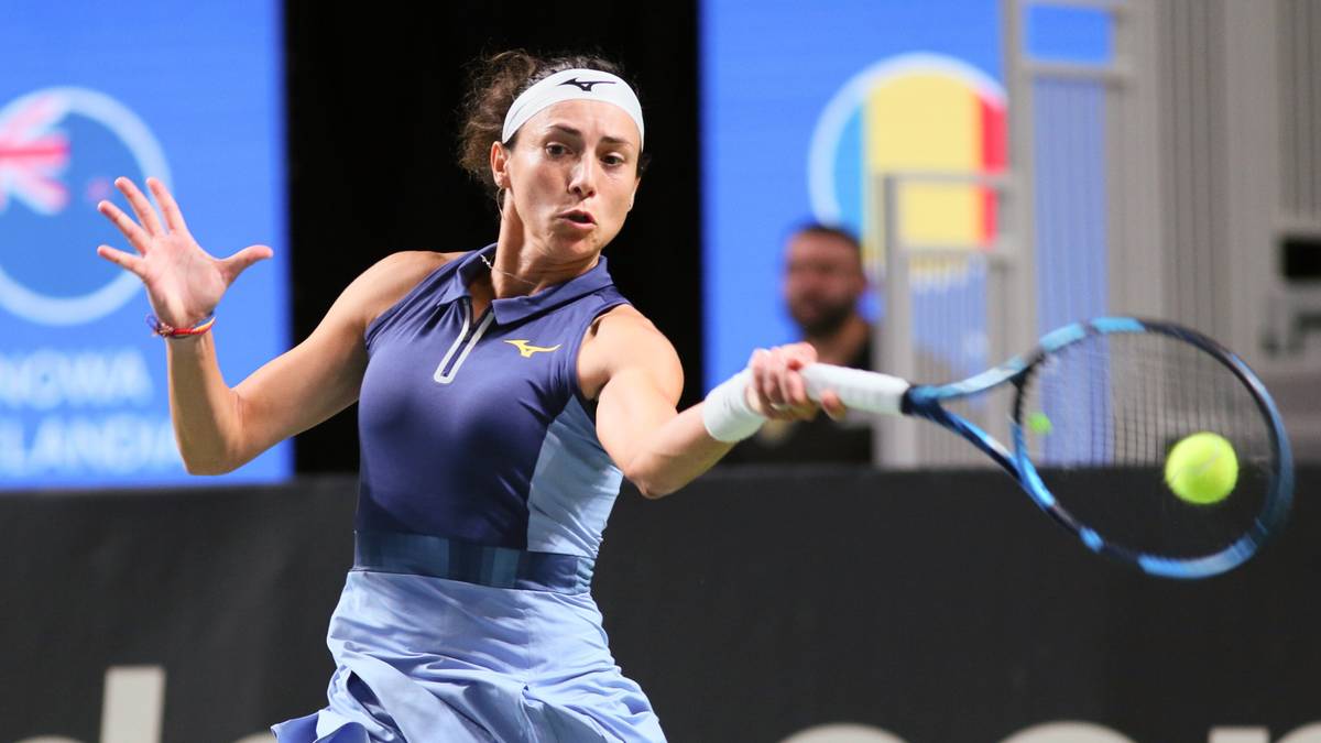 Zawodniczka tenisa Iga Świątek odbija piłkę podczas meczu, ubrana w granatowo-niebieski strój sportowy.