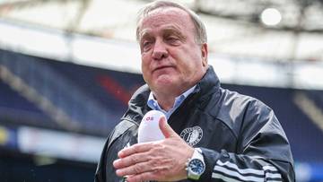 Dick Advocaat, holenderski trener piłkarski, trzymający mikrofon w dłoni, stojący na tle stadionu.