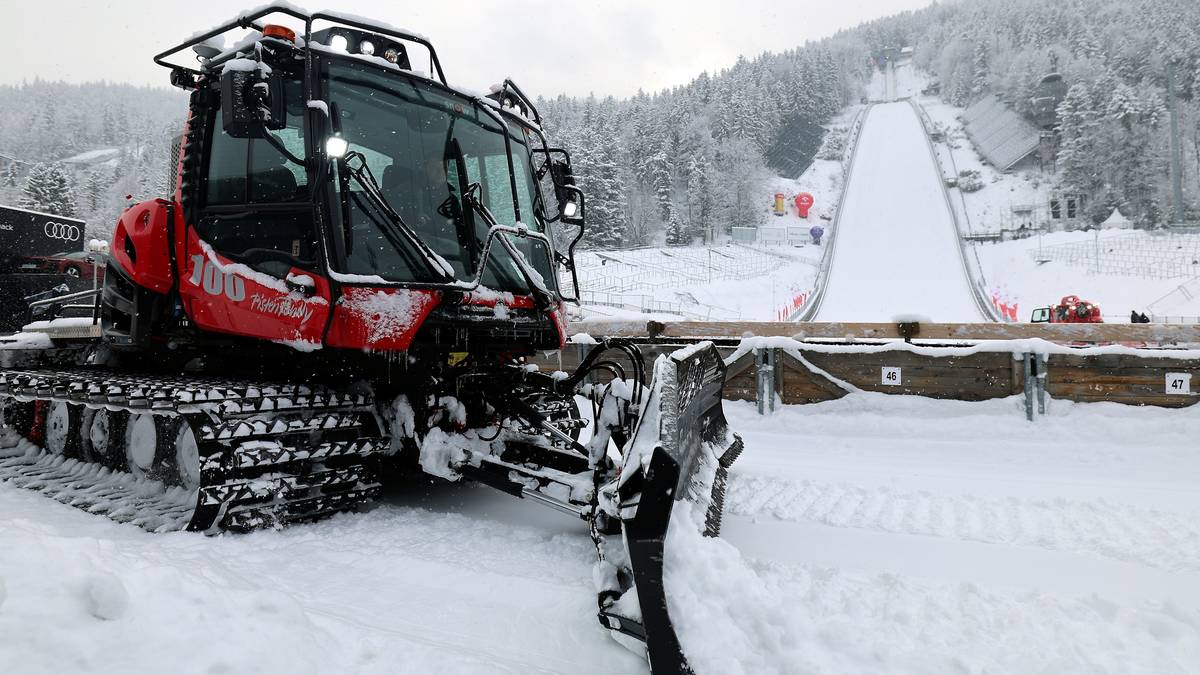 Czerwony ratrak zbliża się do skoczni narciarskiej pokrytej śniegiem.