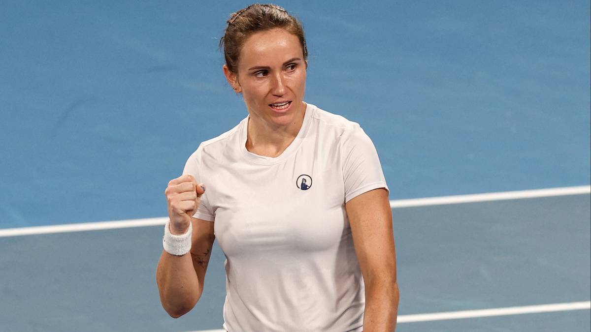 Tenisistka w białej koszulce i czerwonej sp&oacute;dniczce, zaciśniętą pięścią i rakietą w dłoni, świętująca na korcie.