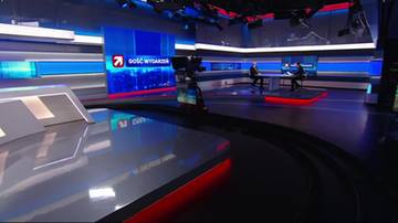 Studio telewizyjne z nowoczesnymi elementami wystroju, w tym dużymi ekranami z logo "Gość Wydarzeń". Widać r&oacute;wnież st&oacute;ł prezydialny z dwoma siedzącymi osobami.