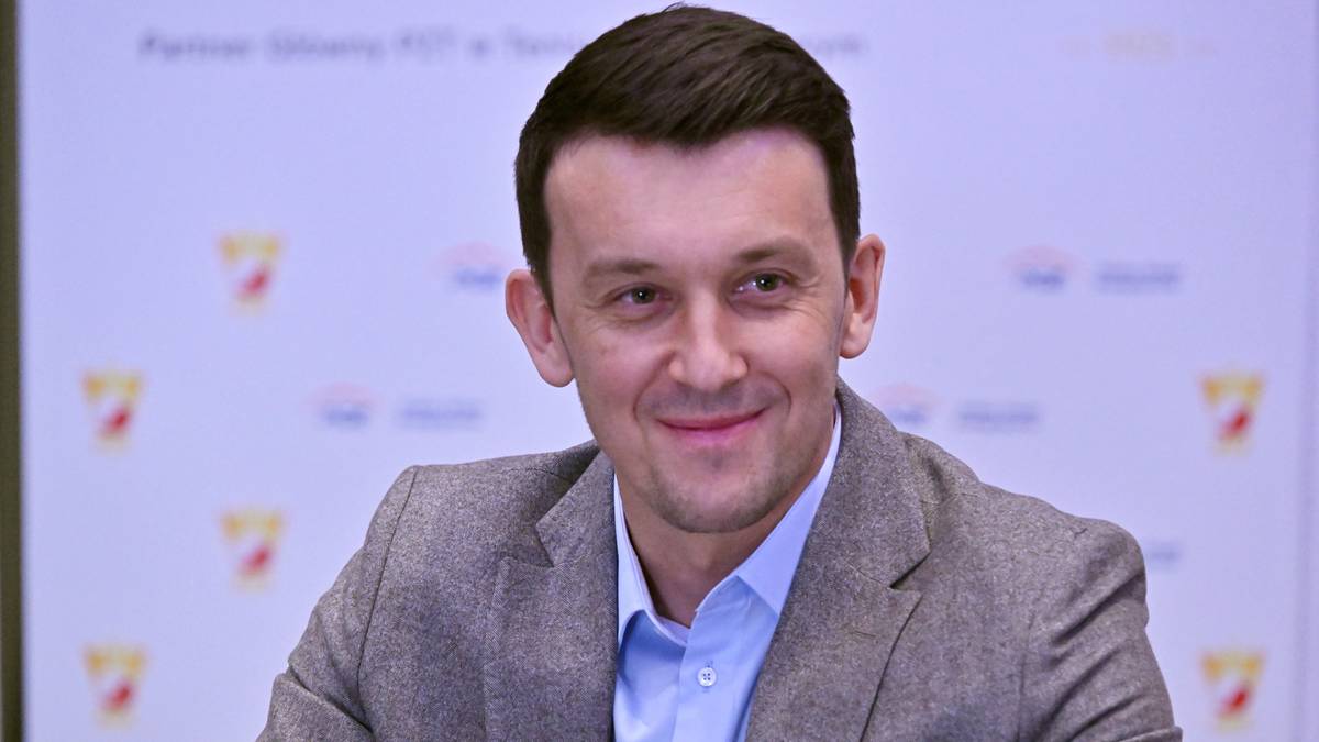 Mężczyzna w garniturze uśmiecha się siedząc podczas konferencji prasowej.