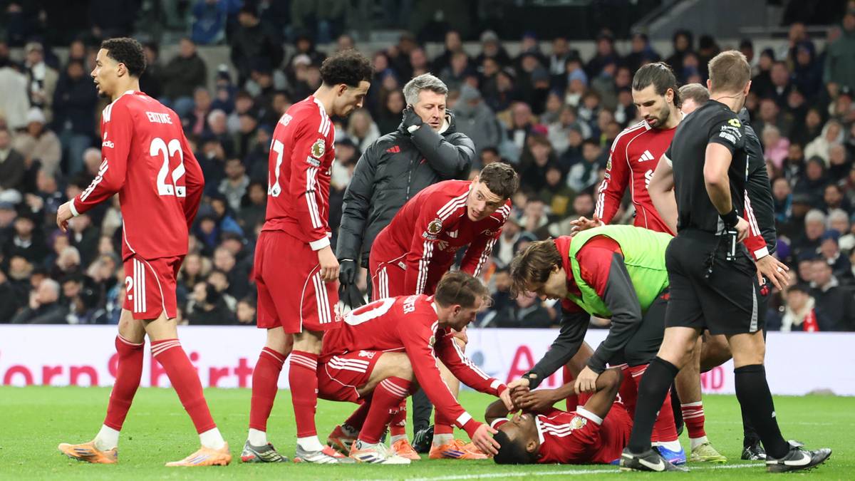 Grupa piłkarzy otacza leżącego na murawie kolegę z drużyny, kt&oacute;remu udzielana jest pomoc medyczna.