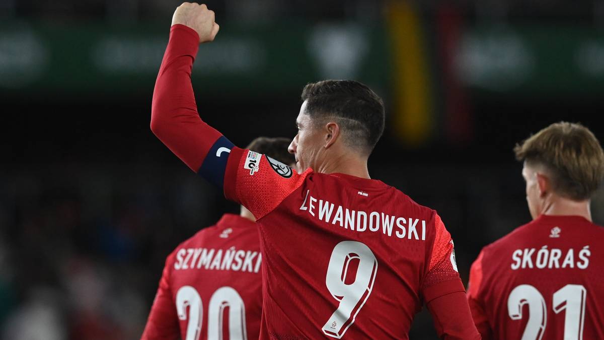 Piłkarz Robert Lewandowski w czerwonej koszulce z numerem 9 i napisem "LEWANDOWSKI" świętuje bramkę, podnosząc prawą rękę z zaciśniętą pięścią.