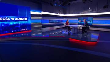 Dwie osoby siedzą przy stole w nowoczesnym studiu telewizyjnym, prowadząc rozmowę.