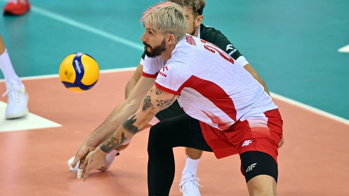 Siatkarz w białej koszulce z czerwonymi elementami broni piłkę rękami.