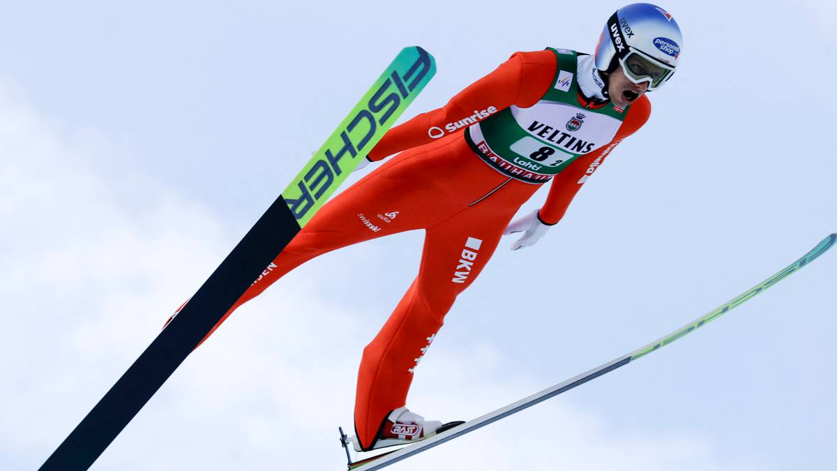 Skoczek narciarski w czerwonym kombinezonie w locie, z nartami Fischer.